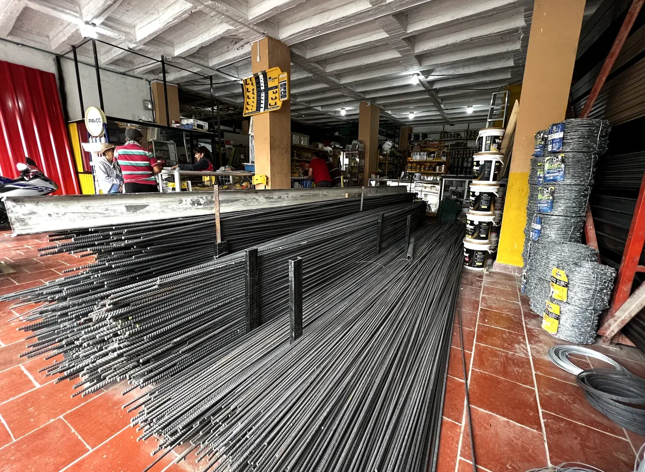 Interior del almacén abierto con varilla corrugada, pinturas y clientes atendidos en el mostrador